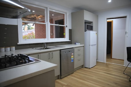 A modern kitchen with a gas stove, dishwasher, refrigerator, and a window overlooking a brick wall.. Convenient Glenroy Accommodation Ideal for Airport Travellers