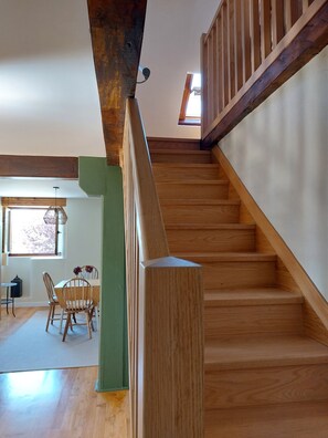 Una escalera de madera con un muro verde decorativo y un área de comedor con mesa y sillas.