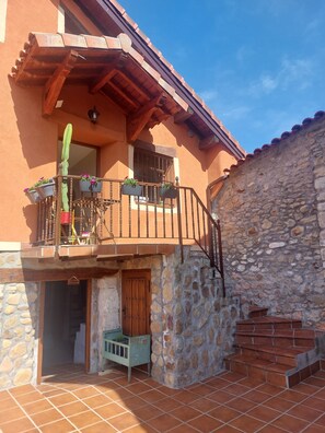 Un edificio de dos pisos con balcón, paredes de piedra y puerta de madera.