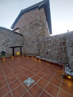 A courtyard with stone walls, a tiled floor, and a small drainage grate.