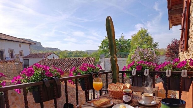 En balkong med ett bord dukat för frukost, med bröd, smör och något att dricka.