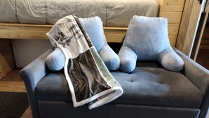 A dark grey sofa with a blanket and pillows, a wooden floor, and a wooden wall.