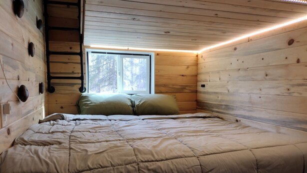 A wooden cabin bedroom with a bed, a window, and a ladder.