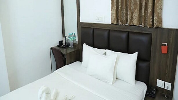 Habitación de hotel con cama, mesita de noche con espejo, lámpara y toalla.
