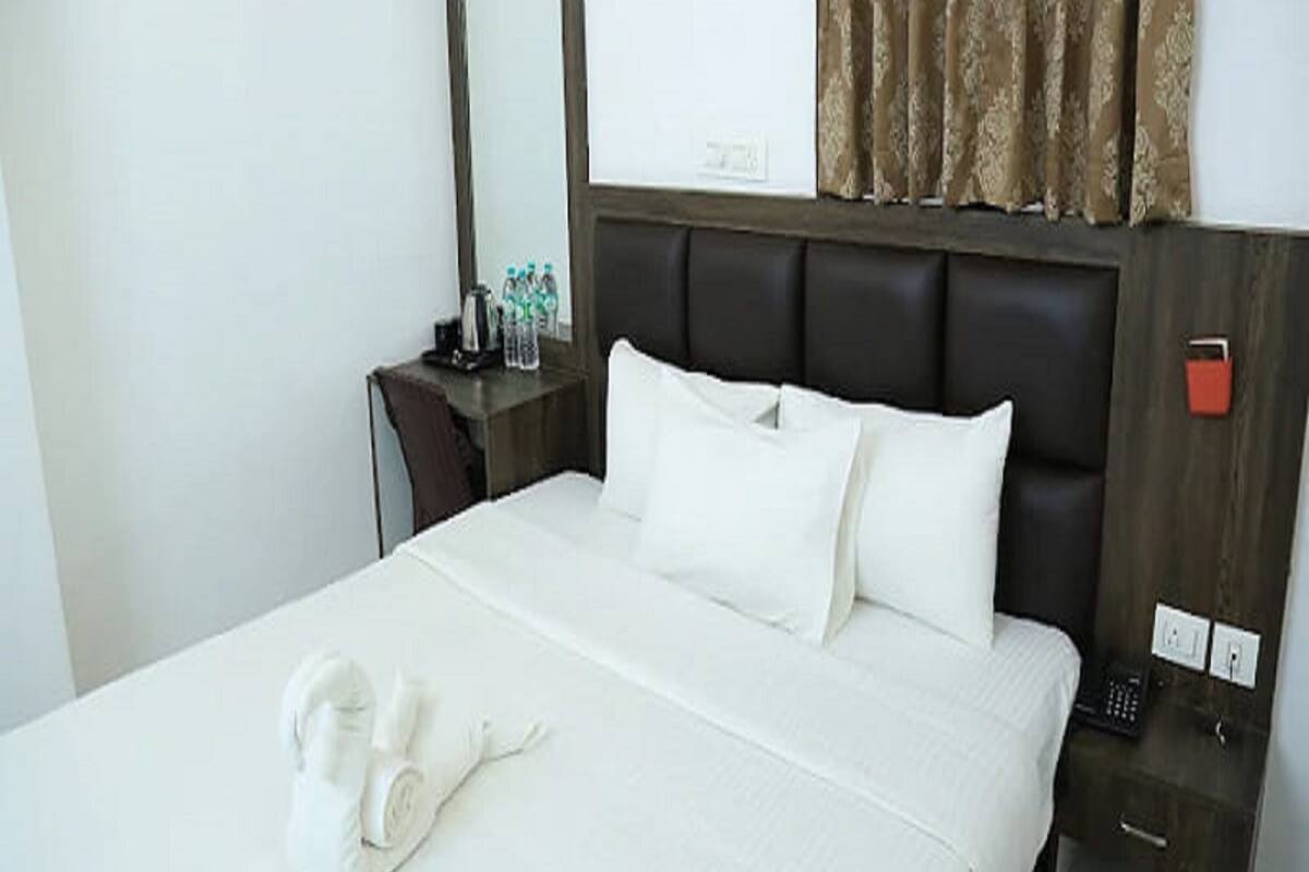 Habitación de hotel con cama, mesita de noche con espejo, lámpara y toalla.