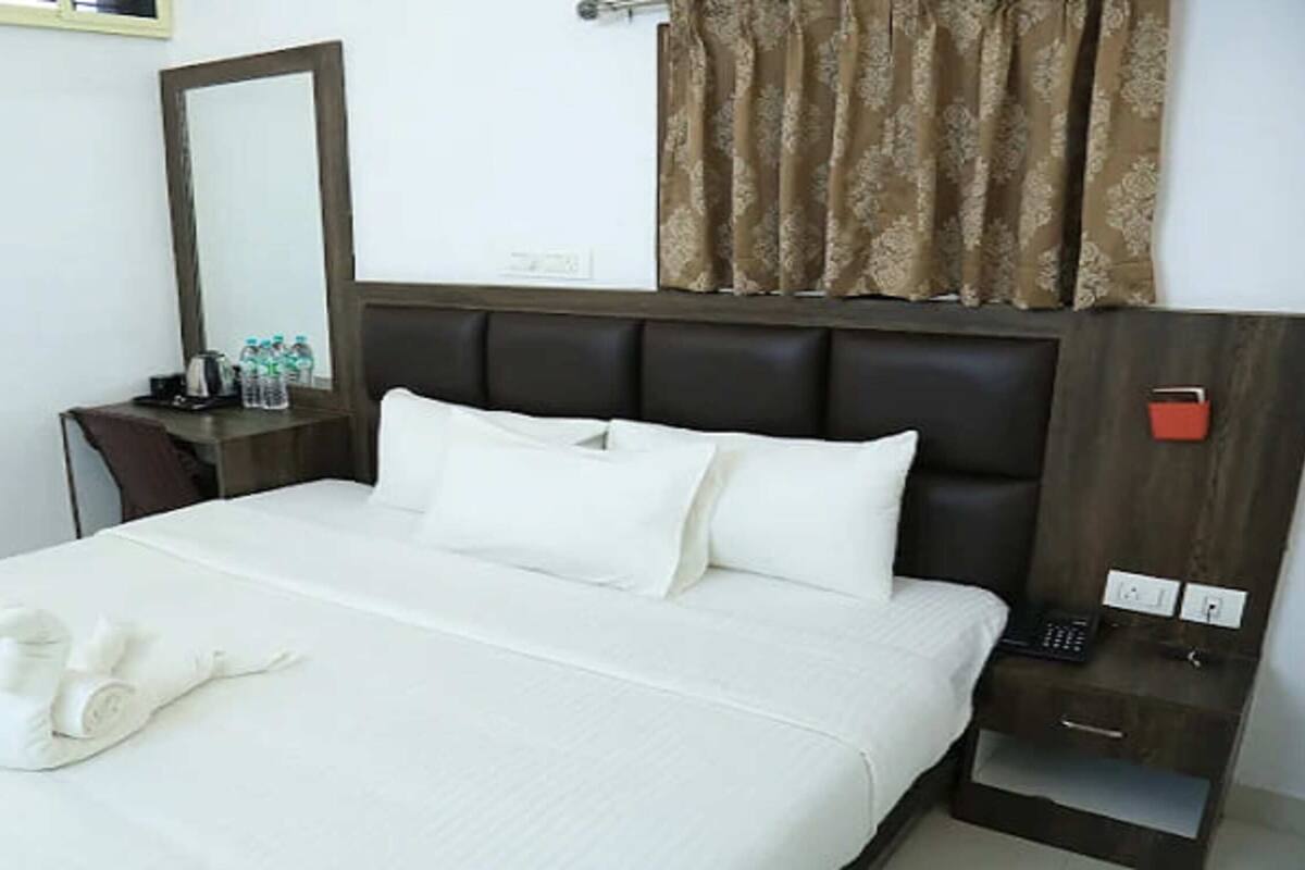 Habitación de hotel con cama, mesita de noche con teléfono, espejo y ventana con cortinas.