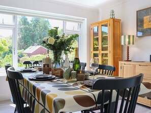 A dining area with a table set for six, a vase with flowers, and a cabinet with glass doors. - 3 bedroom accommodation in Torquay (Torquay)