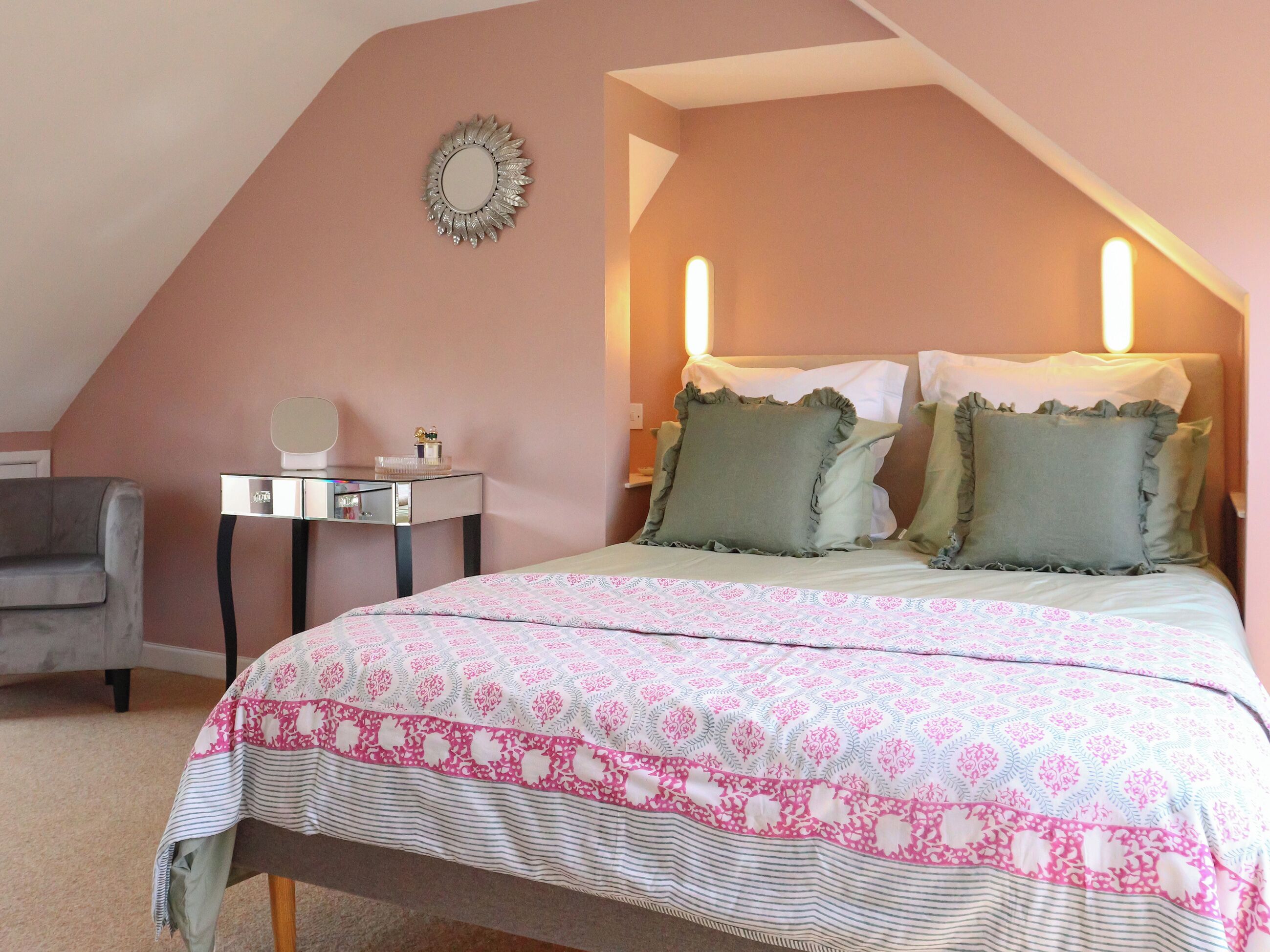 A bedroom with a bed, bedside lamps, a dresser, and a mirror on the wall.