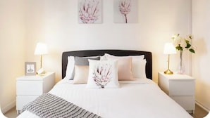 Ein ordentlich eingerichtetes Schlafzimmer mit einem Bett, zwei Nachttischen und Wandbildern.