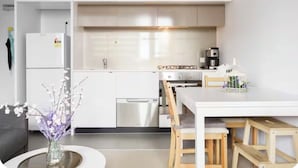 Eine moderne Küche mit weißen Schränken, einem Edelstahl-Kühlschrank, einer Kaffeemaschine und einem Essbereich mit weißem Tisch und Holzstühlen.