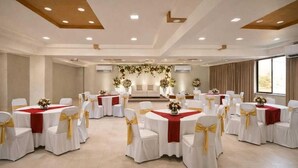 Ein Festsaal mit runden Tischen, weißen Stühlen mit goldenen Bändern und einem Blumenschmuck im Hintergrund.