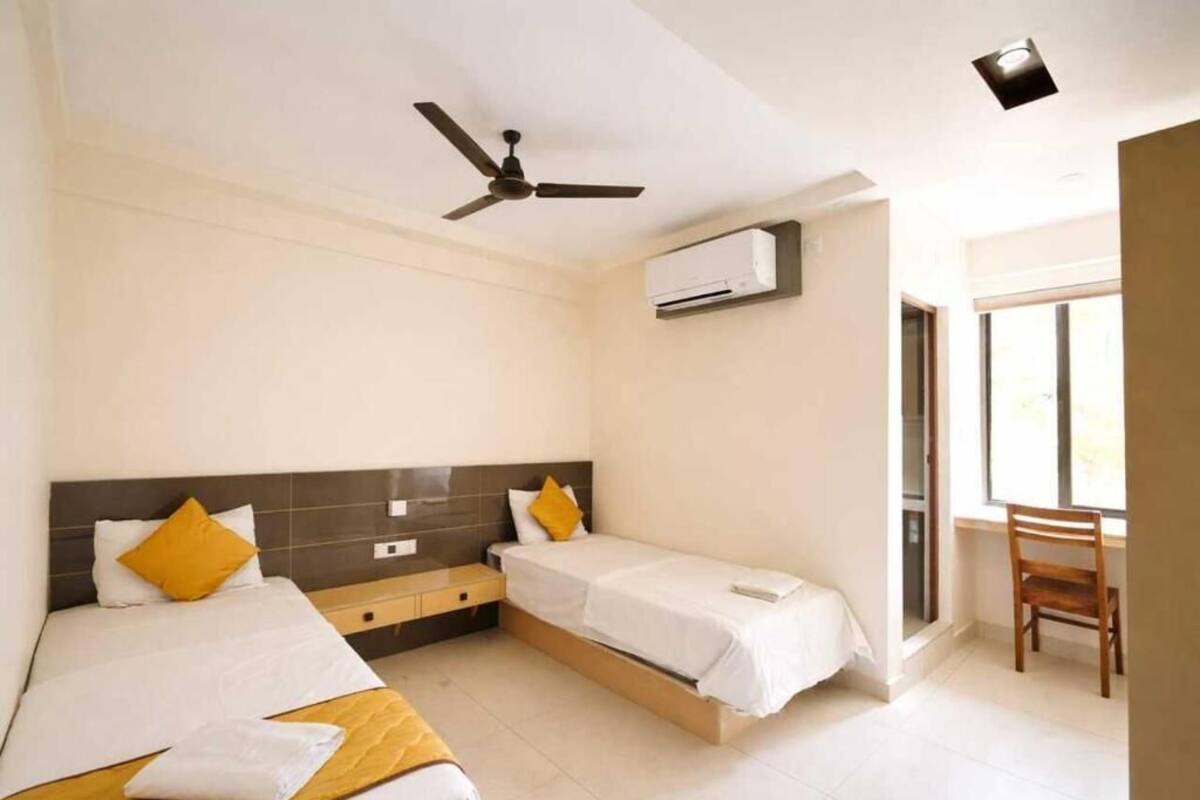 Habitación de hotel con dos camas, ventilador de techo, aire acondicionado y una ventana.