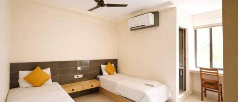 A hotel room with two beds, a ceiling fan, an air conditioning unit, and a window.