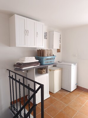 Un espace dédié à la lessive, comprenant un lave-linge, un étendoir et un panier à linge bleu placé sur une étagère.
