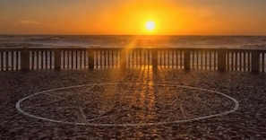 A cobblestone promenade with a wooden railing, leading to the sea at sunset.