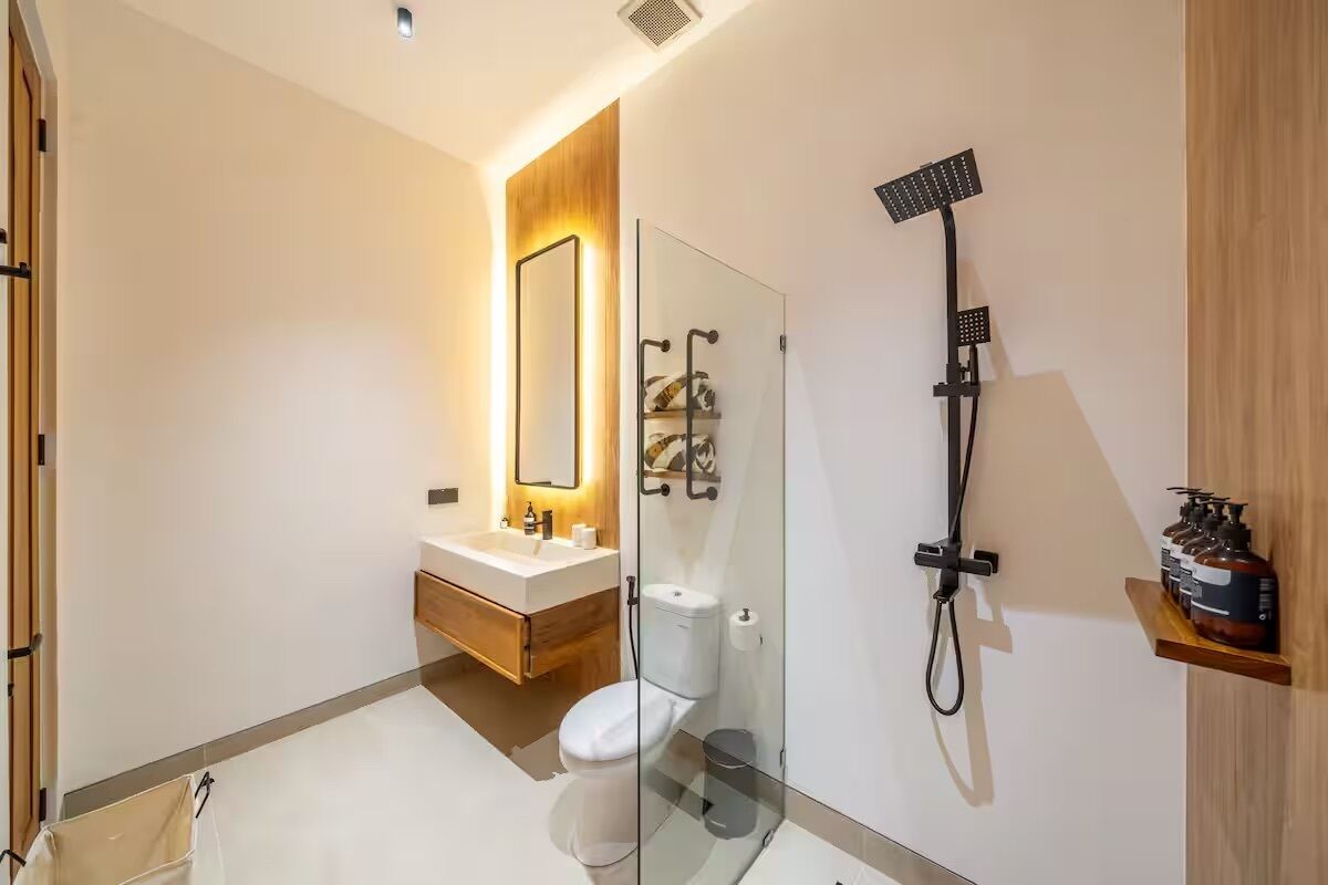 A modern bathroom with a glass shower enclosure, a wooden vanity, and a toilet.