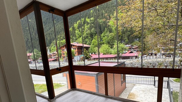 Una habitación con balcón, ventanas amplias y vistas a una zona montañosa con edificios.