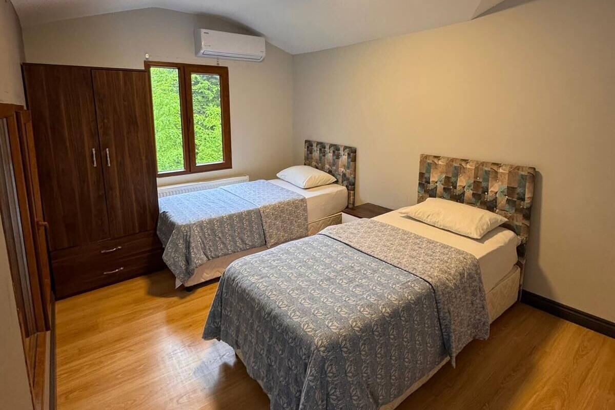 A bedroom with two beds, wooden flooring, a wardrobe, and a window with a view.