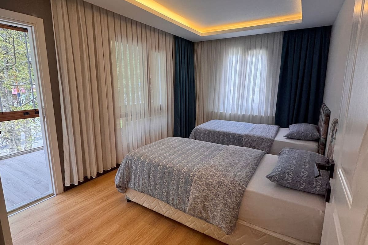 A modern bedroom with two beds, a sliding glass door, and a ceiling light.