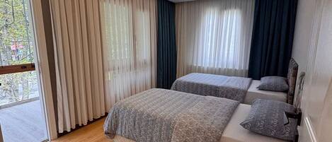 A modern bedroom with two beds, a sliding glass door, and a ceiling light.