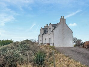 A two-story house with a prominent chimney, surrounded by overgrown vegetation and a wire fence. - Fabulous loch views to the Cuillin mountains. (Roag, near Dunvegan)
