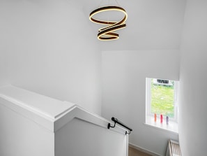 A modern interior with a white staircase, a black handrail, and a window with a view of a green lawn.