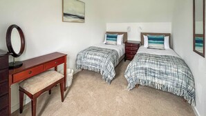 Een slaapkamer met twee bedden, een bureau, een spiegel en een schilderij aan de muur.