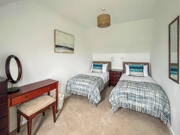 A bedroom with two beds, a desk, a mirror, and a painting on the wall.