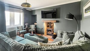 Een moderne woonkamer met een bank, fauteuils, een salontafel, een open haard en een aan de muur bevestigde televisie.