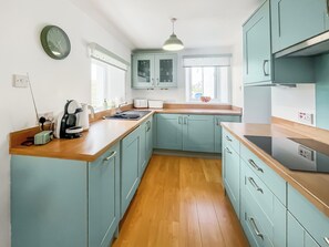 A kitchen with light blue cabinets, a wooden countertop, a sink, a kettle, and a clock on the wall.