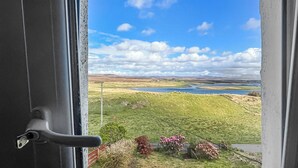 Een deur met uitzicht op een landschap, inclusief een wateroppervlak, groene velden en heuvels.