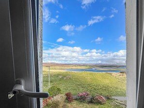 A door with a view of a landscape including a body of water, green fields, and hills.