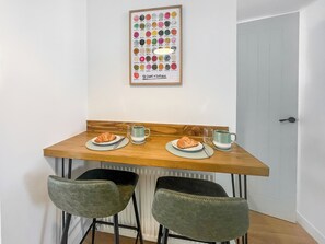 A small dining area with a wooden table, two chairs, a framed picture of Scottish whisky, and a door in the background.
