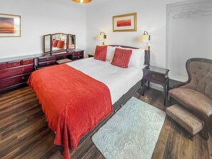 Ett hotellrum med en stor säng, en byrå, en stol och två vägglampor.