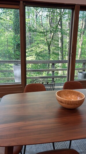 A dining table with a wooden bowl, a chair, and a view of a forest through large windows. - La Cabaña - 3/2 - Secluded Woodland Retreat in Decatur – Minutes from Atlanta (Decatur)