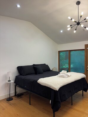 A bedroom with a bed, a bedside lamp, a ceiling light fixture, and a window with a view of trees. - La Cabaña - 3/2 - Secluded Woodland Retreat in Decatur – Minutes from Atlanta (Decatur)
