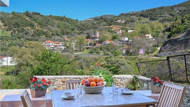Una mesa de comedor con sillas, un cuenco de fruta y una vista a una colina con casas.