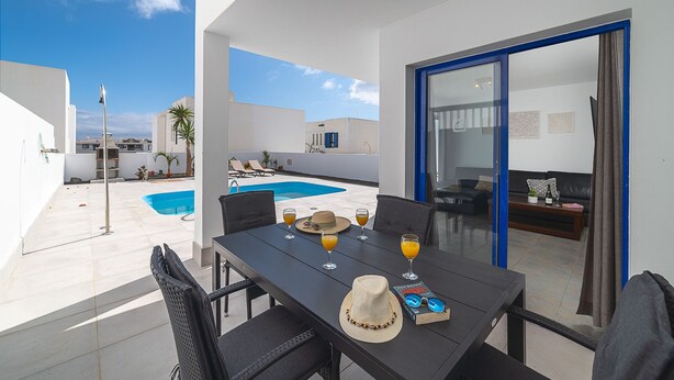 Ein Essbereich mit Tisch für vier Personen, einem Pool und Blick auf die umliegenden Gebäude.