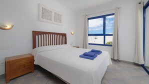 Ein Schlafzimmer mit Bett, Nachttisch, Wandbild und einem Fenster mit Vorhängen.