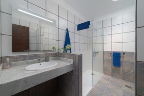 A bathroom with a large mirror, a sink, a shower, and a blue towel hanging on the wall. - Villa Yaiza 10 - VipVipVillas (Playa Blanca)