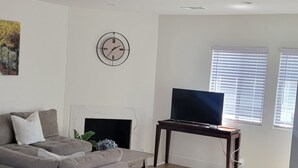 A modern living room with a sofa, a TV on a stand, a fireplace, and a clock on the wall.