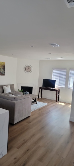 Una sala de estar moderna con un sofá gris, una mesa de centro de madera, un televisor de pantalla plana y un reloj de pared.