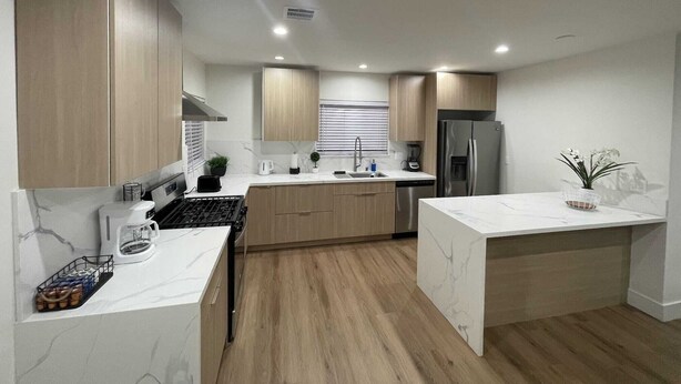 A modern kitchen with wooden cabinets, a stainless steel refrigerator, and a marble countertop.