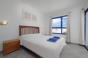 Ein Schlafzimmer mit Bett, Nachttisch, Wandbild und einem Fenster mit Vorhängen.