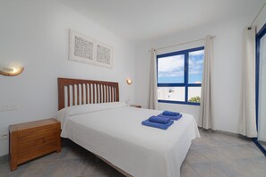 A bedroom with a bed, nightstand, wall art, and a window with curtains. - Villas Yaiza 2 - VipVipVillas (Playa Blanca)