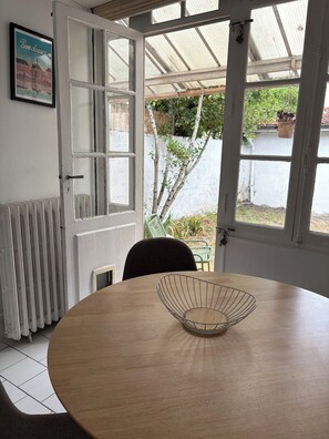 Ein Zimmer mit einem runden Tisch, einem Stuhl, einer Heizung, einer Tür mit Fensterglas und Blick ins Grüne.