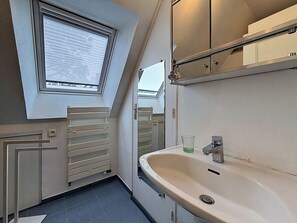Ein schmales Badezimmer mit einem Oberlicht, einem weißen Waschbecken und einem Spiegel darüber.