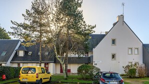 Ein Parkplatz mit einem gelben Lieferwagen und einem silbernen Auto vor einem weißen Gebäude mit geneigtem Dach.