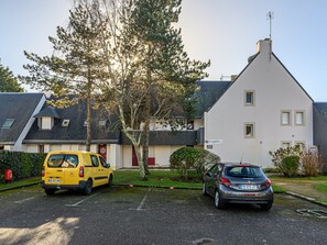 Ein Parkplatz mit einem gelben Lieferwagen und einem silbernen Auto vor einem weißen Gebäude mit geneigtem Dach.