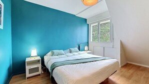 Ein Schlafzimmer mit einem Bett, einem Nachttisch, einer Lampe, einem Fenster und einer Deckenleuchte.